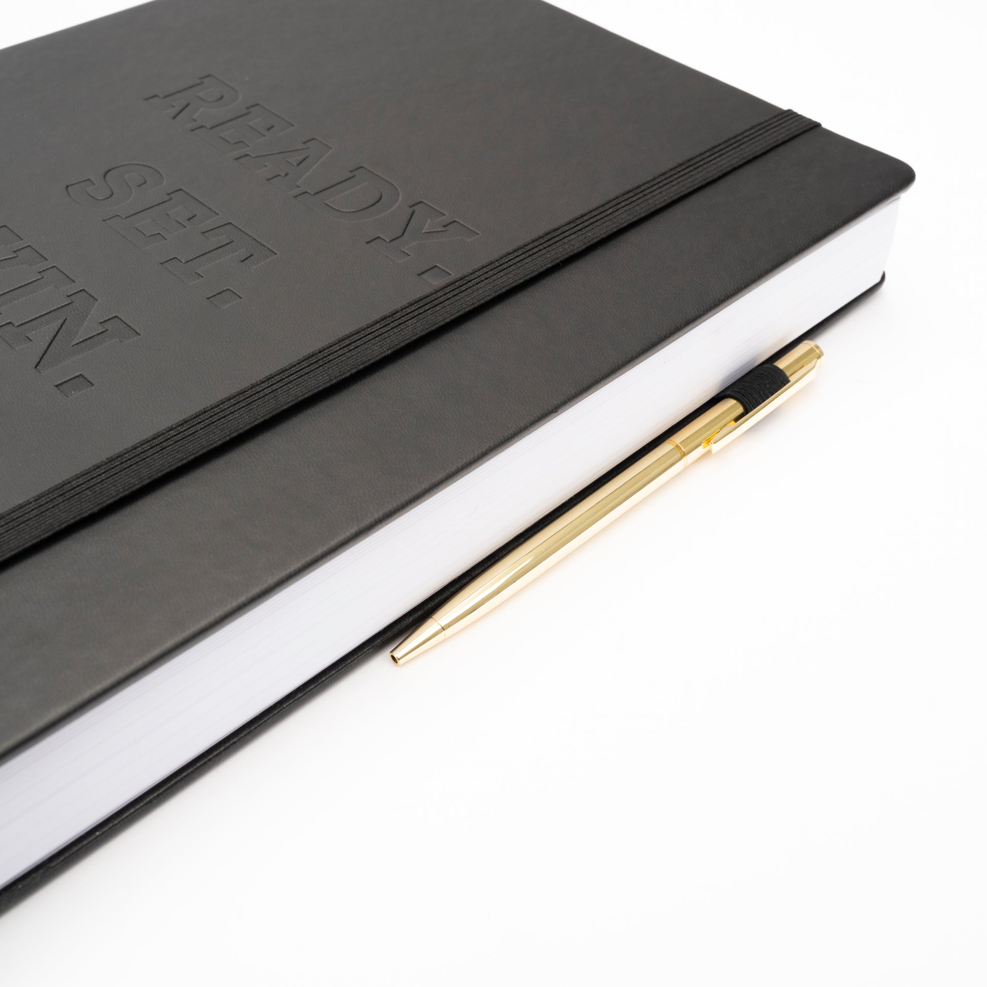 Zoomed in cover of black Ready Set Win 6 Month Planner that is showcasing the elastic band and gold pen in elastic pen holder.
