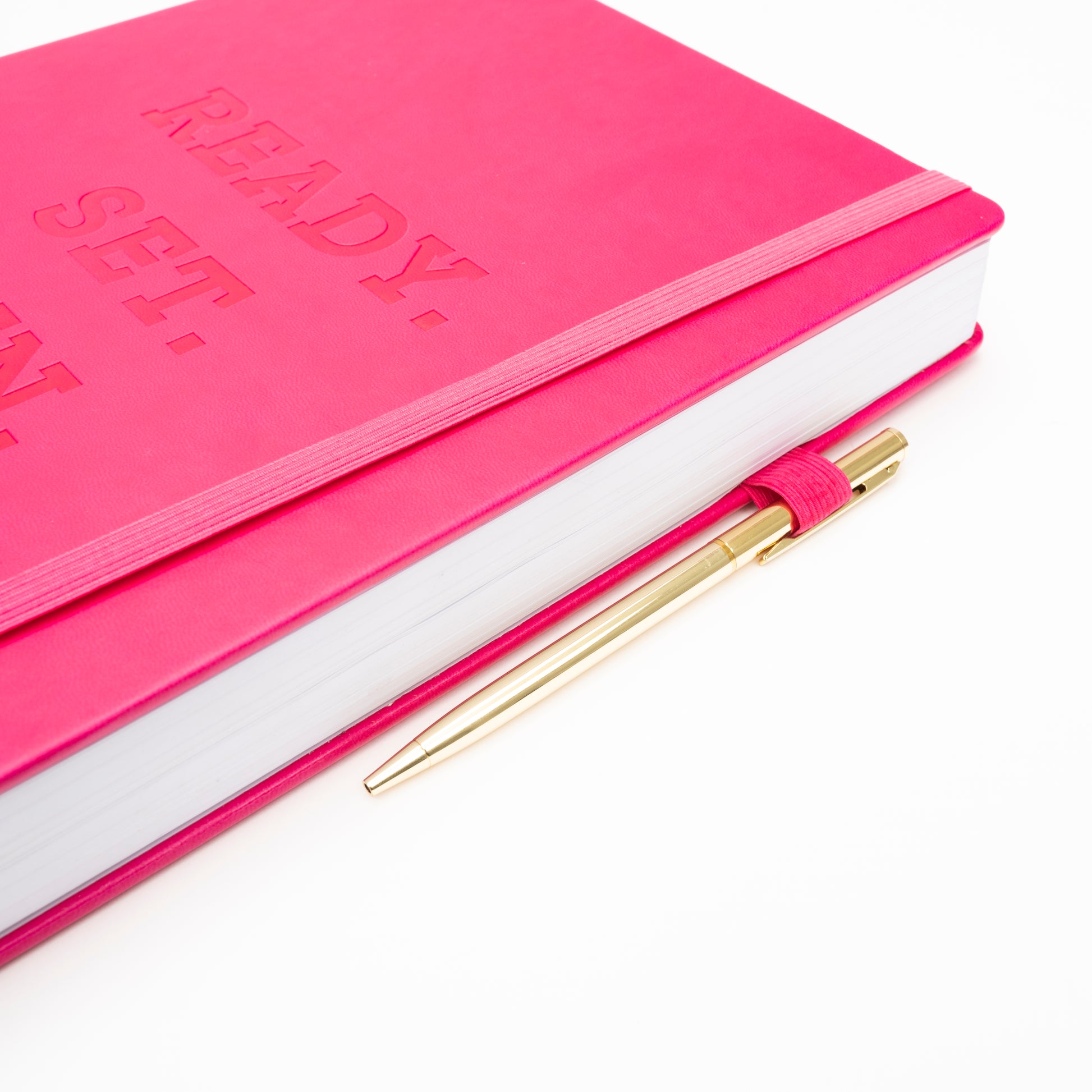 Zoomed in cover of pink Ready Set Win 6 Month Planner that is showcasing the elastic band and gold pen in elastic pen holder.