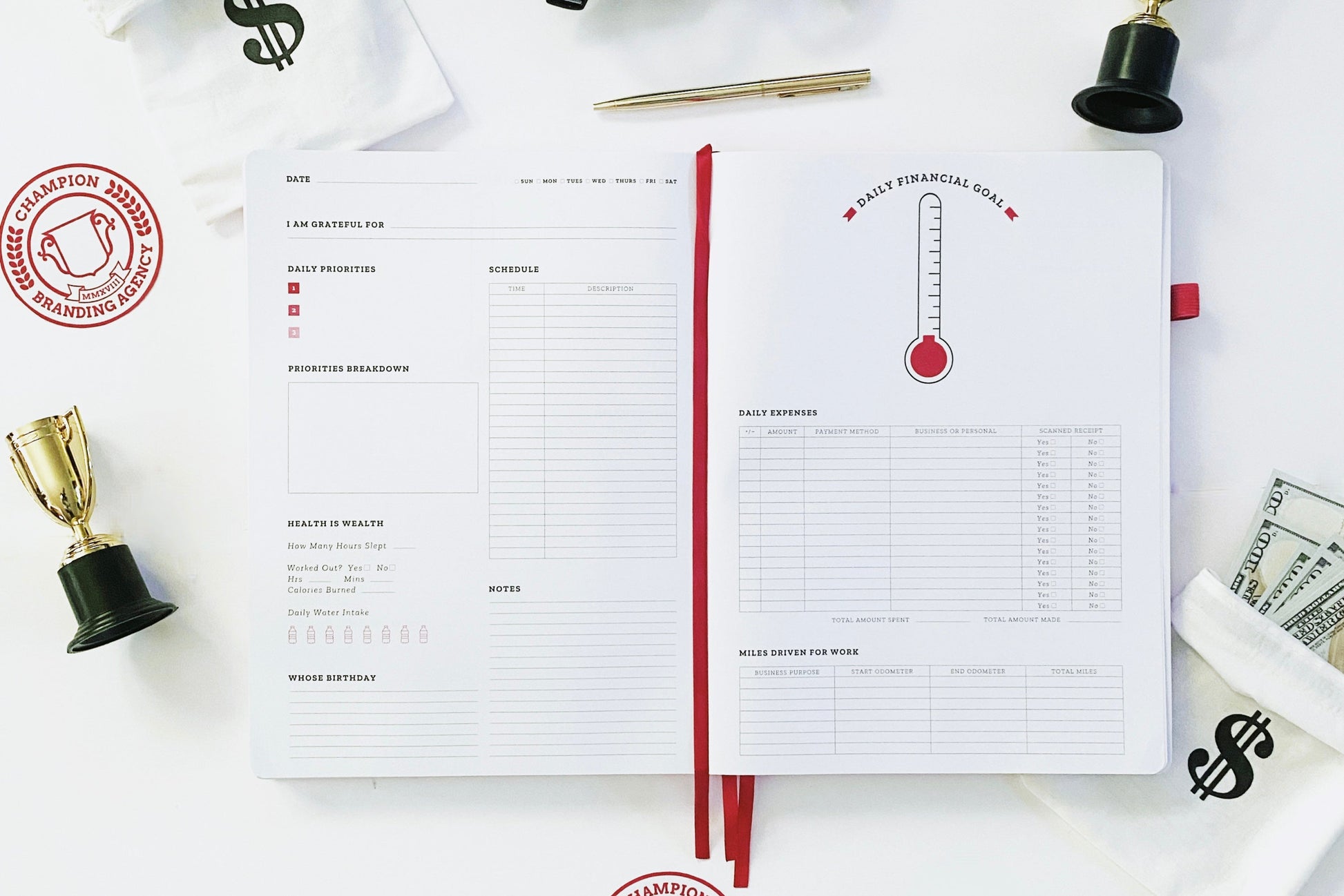 Daily planning page of black Ready Set Win productivity planner. It is flat-laid to the daily page that features dates, a brain dump section, a schedule, a health section, a birthday, notes, and a financial goal page including daily expenses and other features. It is surrounded by small trophies, small money bags with hundred dollar bills, also a gold pen, black frame blue light glasses, and Champion Branding Agency logo stickers.